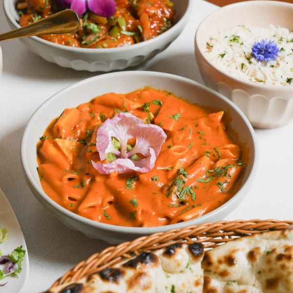 Close-up of Indian butter chicken pasta, rice, and naan bread on a white table.