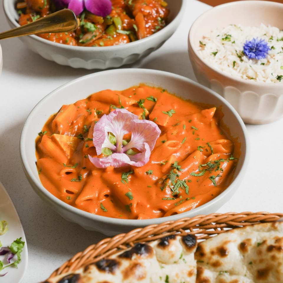 Close-up of Indian butter chicken pasta, rice, and naan bread on a white table.