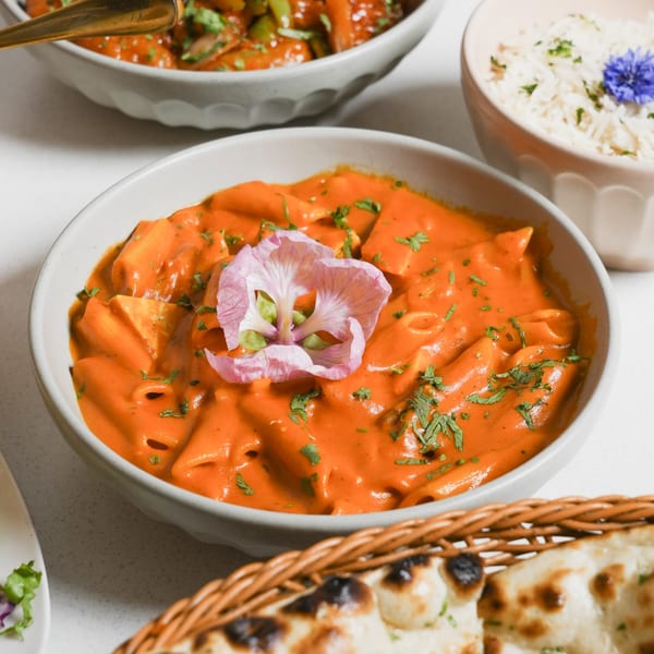 A bowl of Ticca Tikka Indian Cuisine's creamy orange pasta with a pink flower garnish.