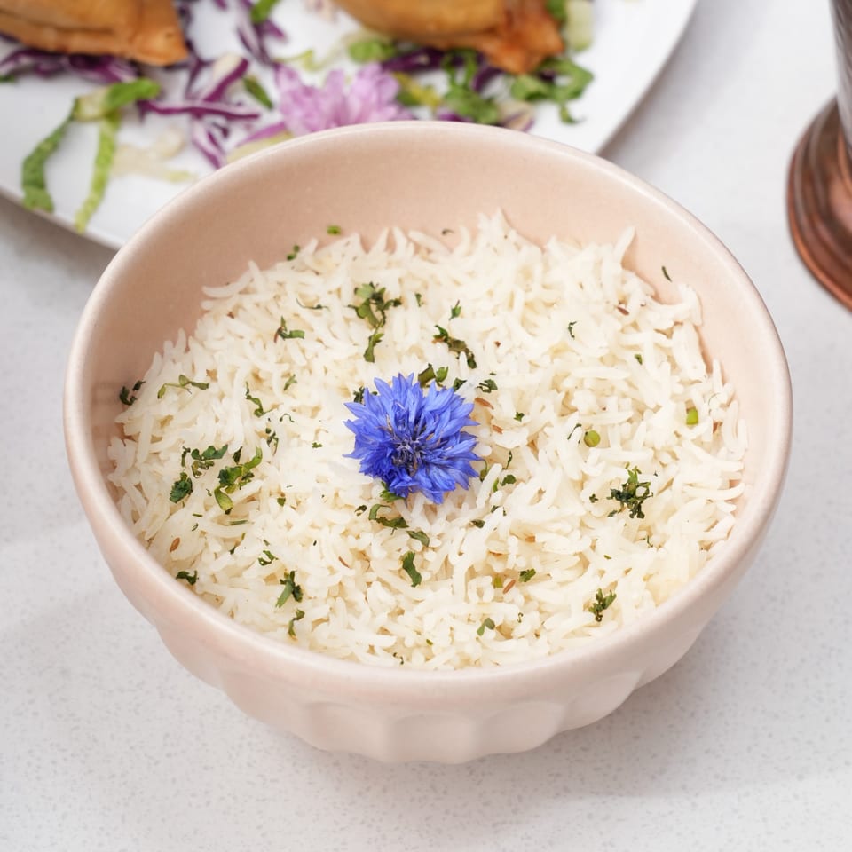 A light pink bowl of white rice, garnished with green herbs and a blue flower.