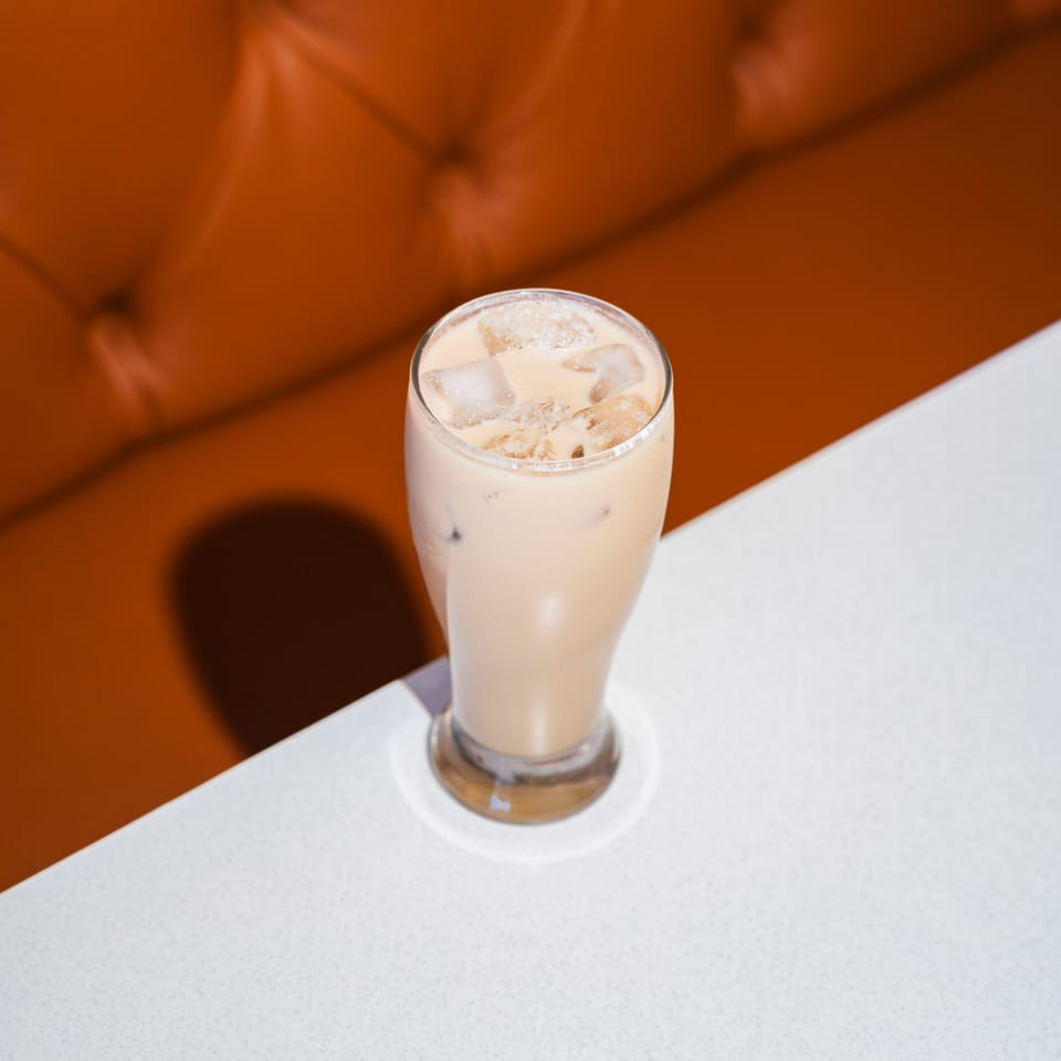 Iced chai latte with ice cubes on a white table, with an orange booth in the background.