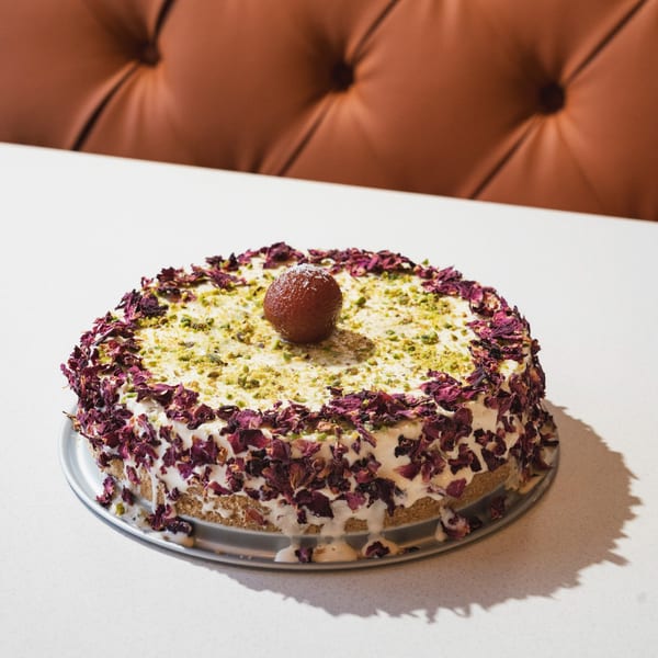 A Gulab Jamun cheesecake, topped with a single Gulab Jamun, pistachios, and dried rose petals.