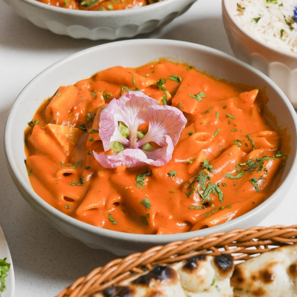 A bowl of Ticca Tikka Indian Cuisine's orange pasta with a pink flower garnish.