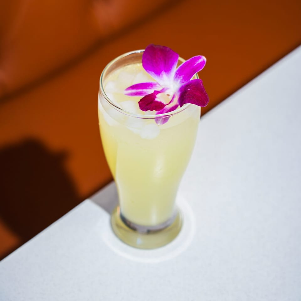 Refreshing yellow drink with ice and a vibrant purple orchid garnish on a white table.