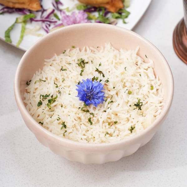 A bowl of white rice garnished with green herbs and a vibrant blue flower.