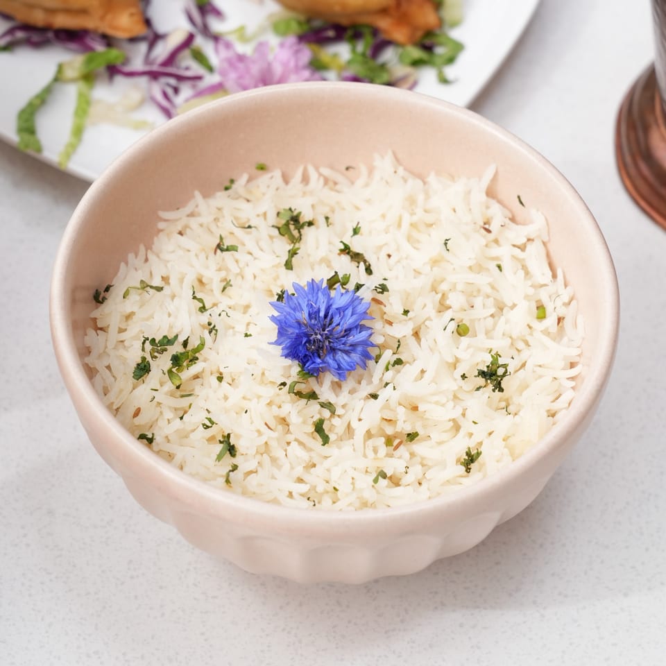 A bowl of white rice garnished with green herbs and a vibrant blue flower.