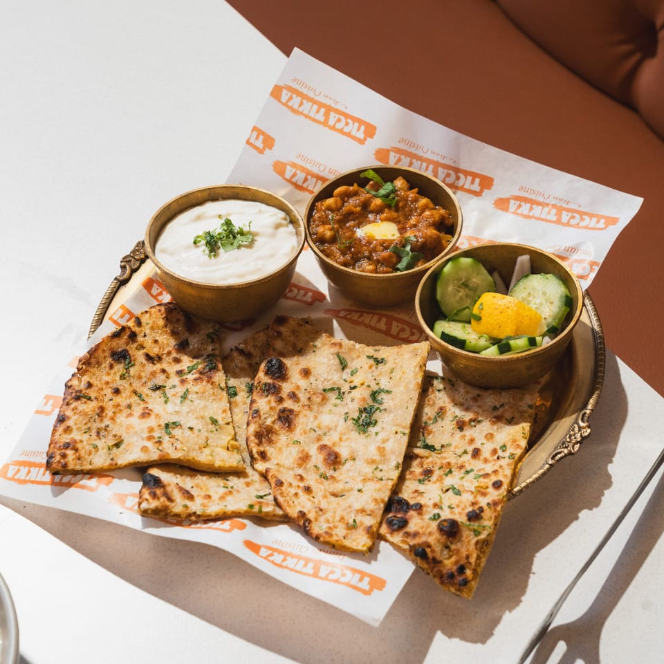 Indian flatbread, chickpea curry, yogurt, and cucumber salad on a gold tray.