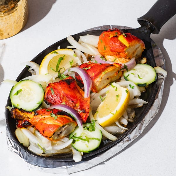 Sizzling Ticca Tikka chicken with onions, lemon, and cucumber on a hot plate.