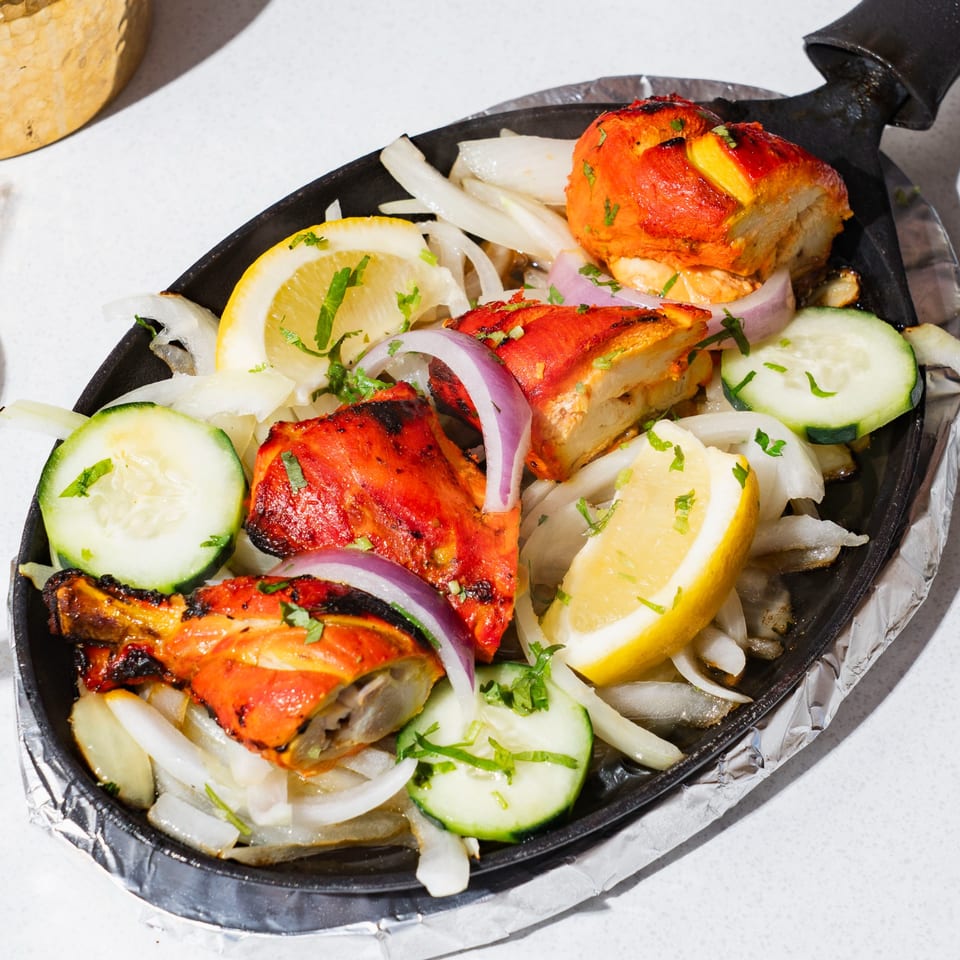 Tikka Tikka Indian Cuisine's Tandoori Chicken, garnished with onions, lemon, and cucumber on a hot plate.