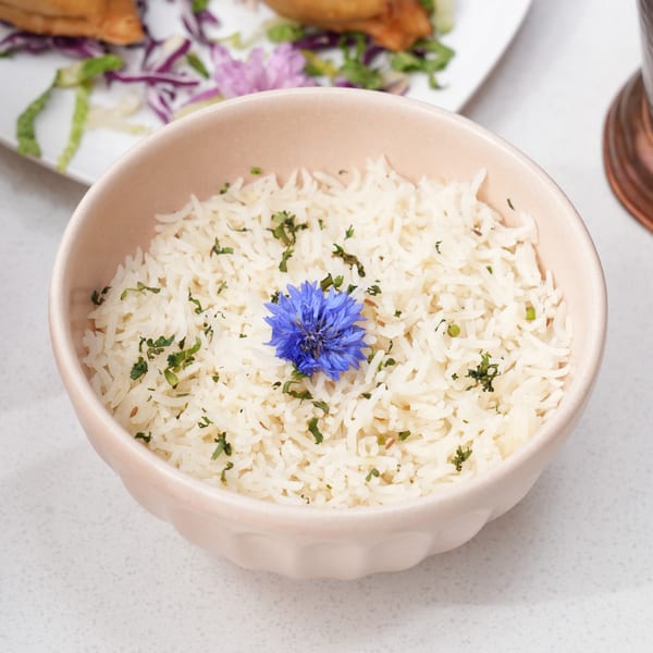 A bowl of white rice garnished with green herbs and a vibrant blue flower.