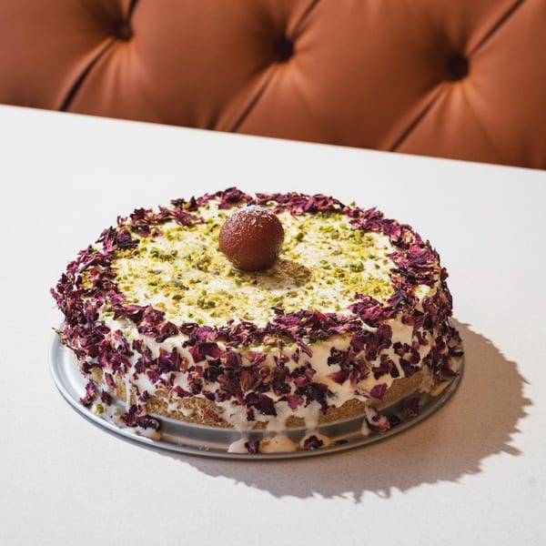 Indian Gulab Jamun cake with rose petals and pistachios on a white table.