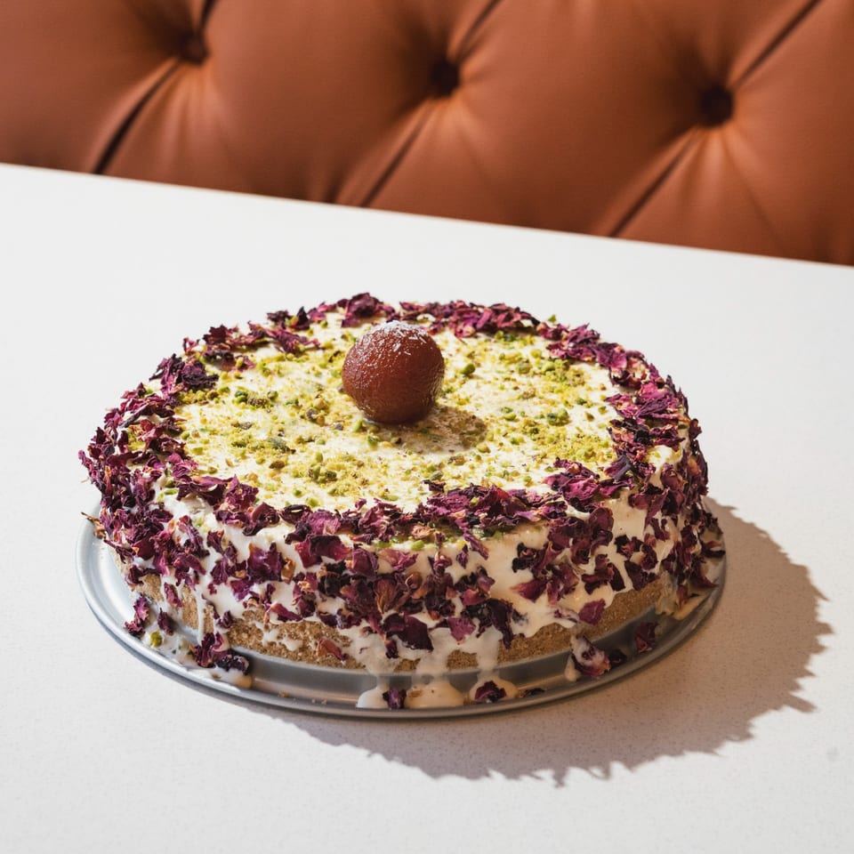 Indian Gulab Jamun cake with rose petals and pistachios on a white table.