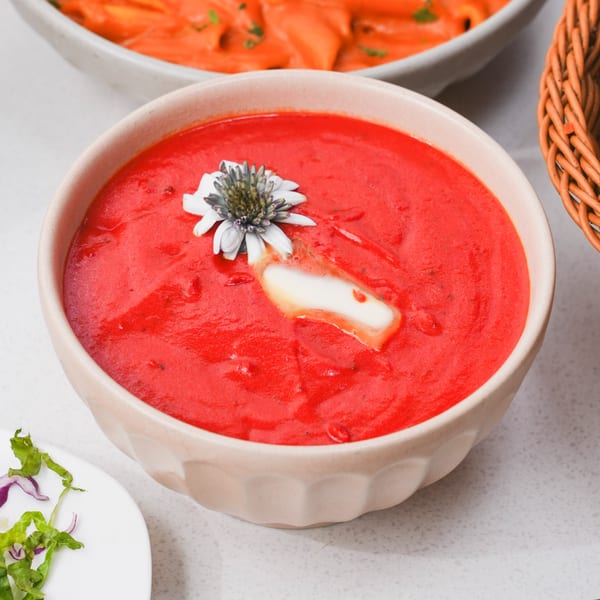 Vibrant red Indian tomato soup in a bowl, garnished with a flower and cream.