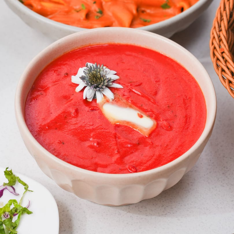 Vibrant red Indian tomato soup in a bowl, garnished with a flower and cream.
